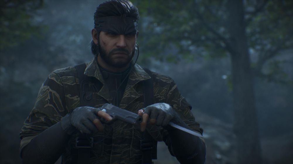 Screenshot of Metal Gear Solid 3 Remake, protagonist Snake stands in a forest, he is wearing a camouflage outfit and is holding a pistol in one hand and a knife in the other 