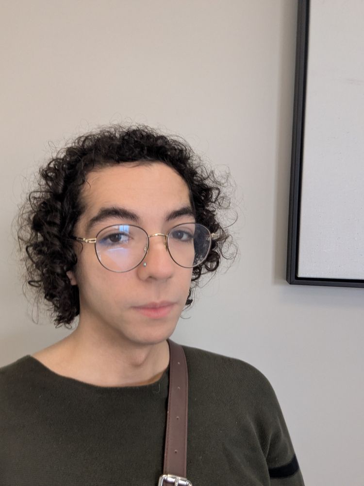 Selfie of me in front of a white wall wearing a dark green shirt