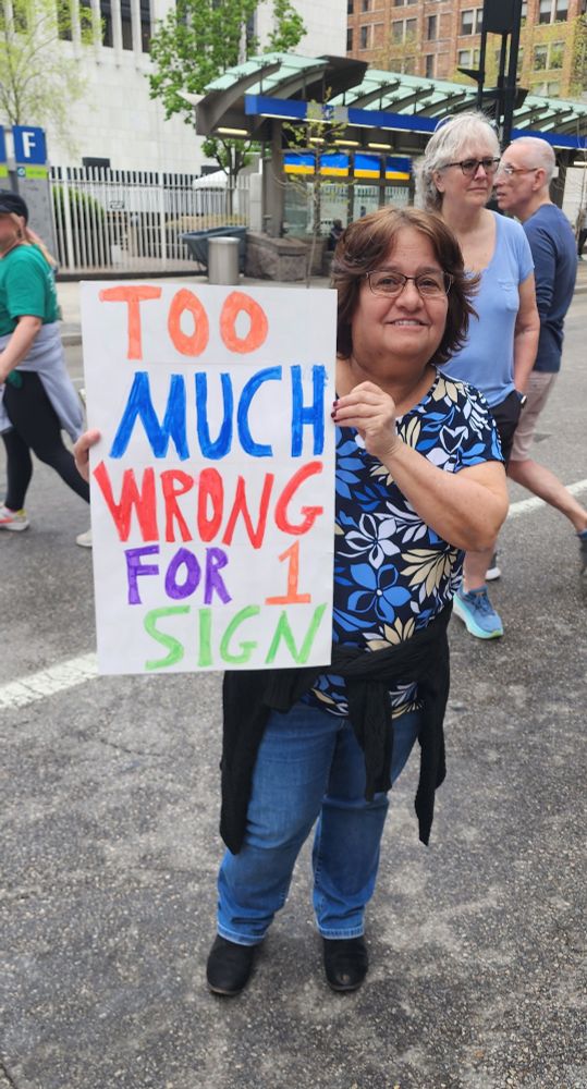 Woman holding a protest sign stating "Too much wrong for 1 sign" in Cincinnati, Ohio 4-19-25