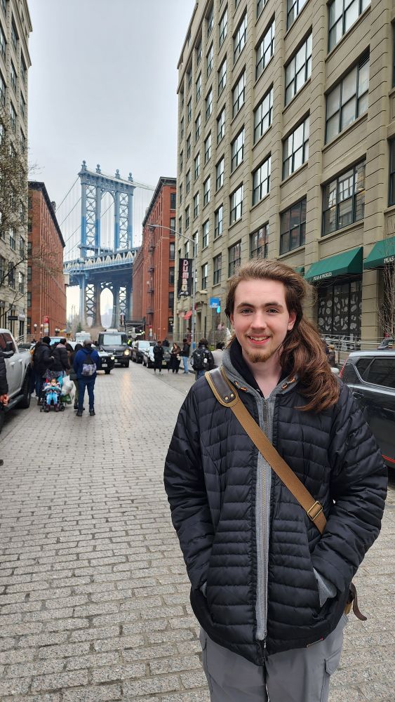 Teenager on the street in Dumbo with a view of the Manhattan Bridge behind him