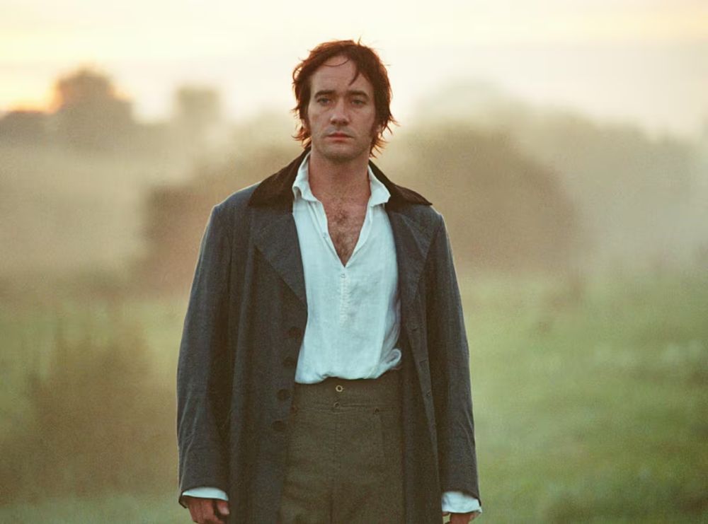 Imagen de Darcy en la adaptación de Orgullo y Prejuicio de 2005, en la que aparece con la camisa abierta, el abrigo descordado y caminando en un prado al alba. 