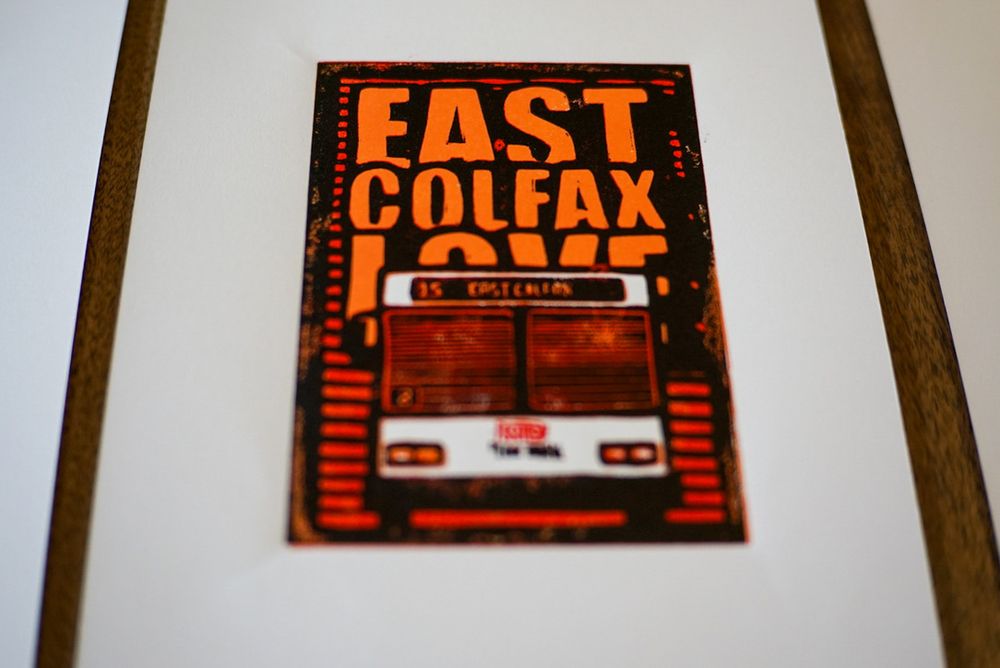 Linocut print, white, light orange, dark orange and black. The front of a RDT 15 East Colfax bus in Denver Colorado. The text reads "East Colfax Love" in all caps. 