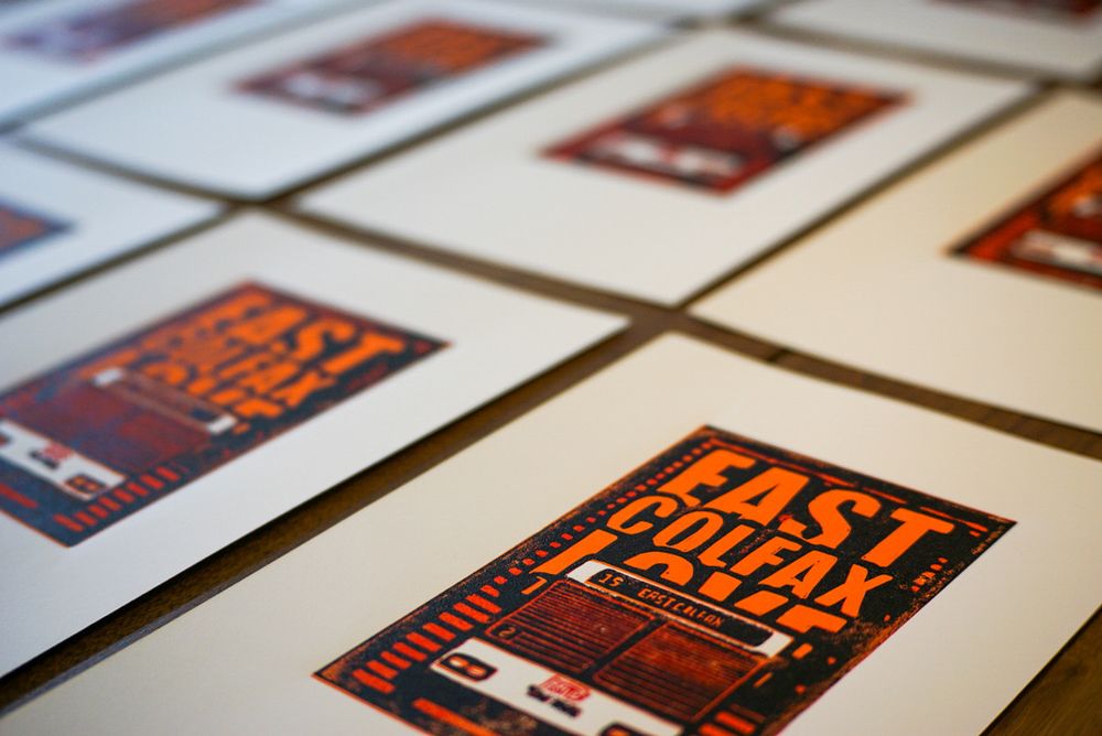 Angled picture of several linocut prints, white, light orange, dark orange, and black. The front of an RDT 15 East Colfax bus in Denver, Colorado. The text reads "East Colfax Love" in all caps. 