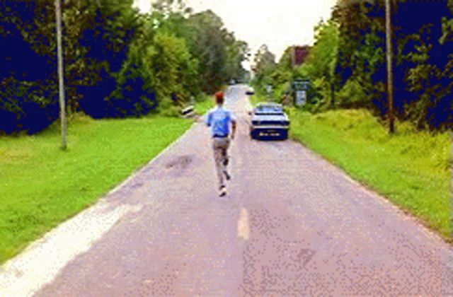 a man in a blue shirt is running down a road with a car in the background