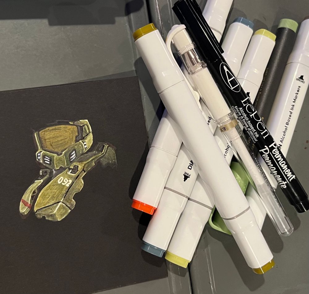 Some markers sit beside an in process, unfinished drawing on black paper of a spartan from halo