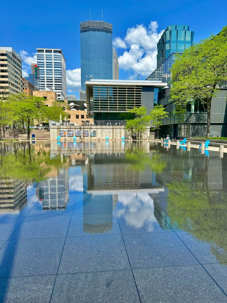 The reflective pool at Peavey Plaza with the Mpls skyline and blue skies in the background.
