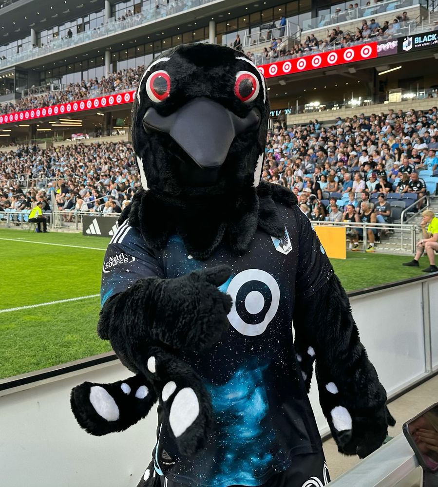 MN United’s mascot PK pointing at the camera with the pitch behind him.