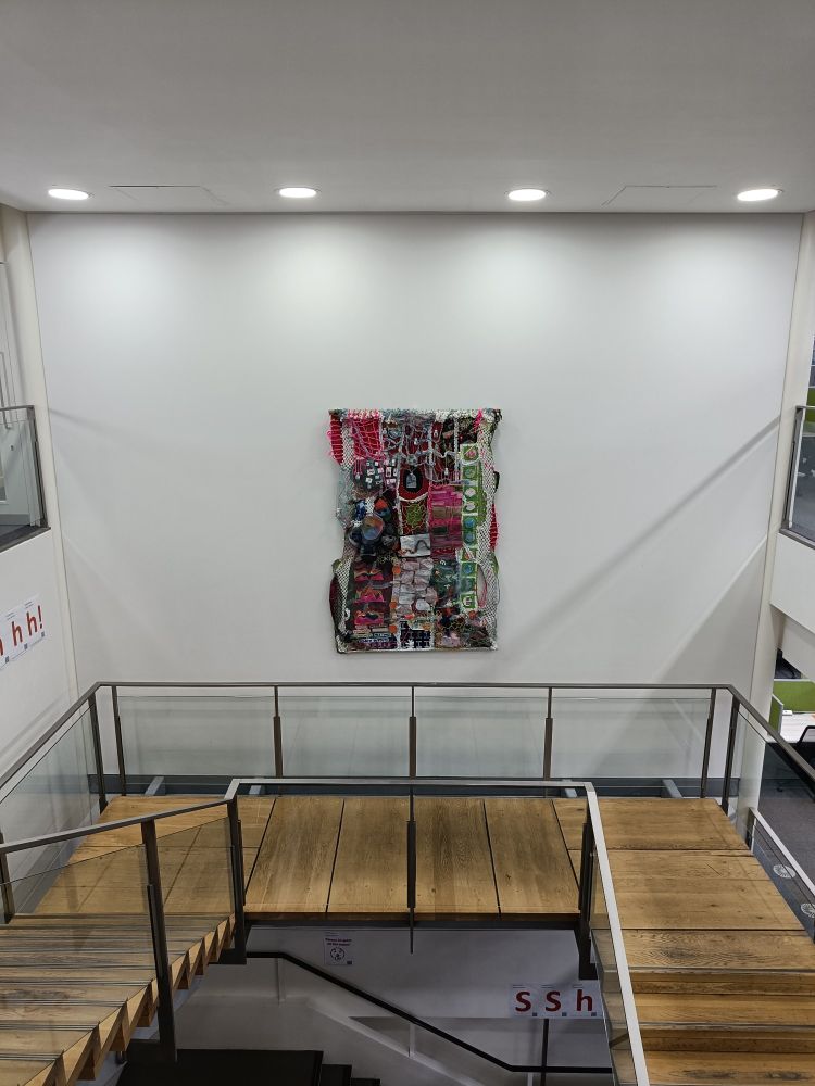 A colourful tapestry made with many different materials exploring themes around science. The tapestry is hung on the walls of a stairwell in the Abdus Salam Library. 