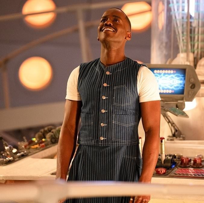 Dr. Who,  inside the tardis, smiles joyfully. Lights of the tardis shine on him. 