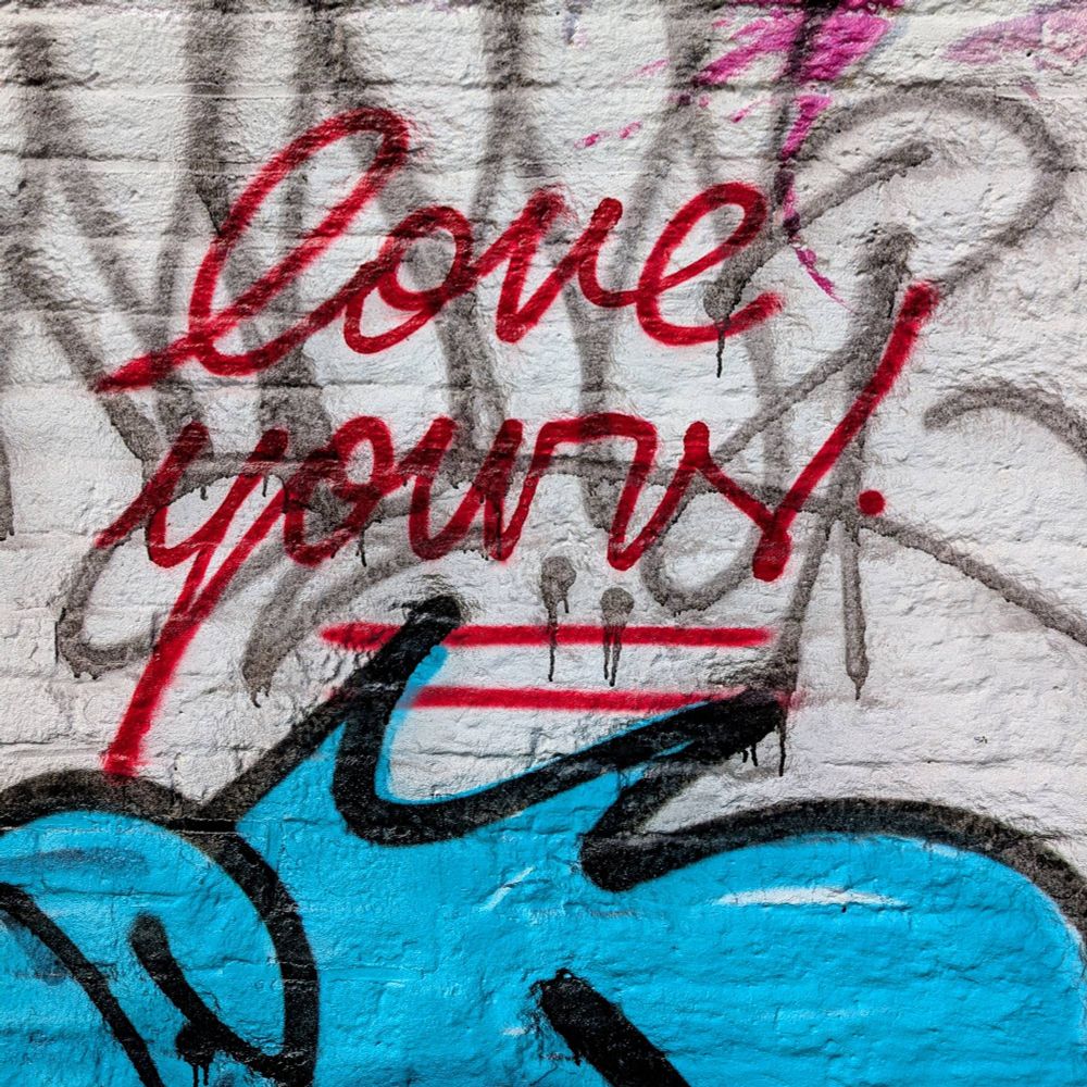 Graffiti on a white brick wall with the text "love yours!" in red