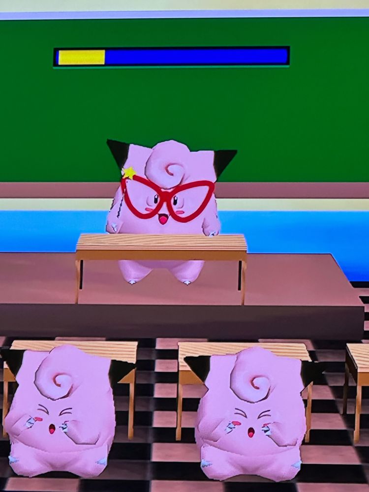 The Pokemon Clefairy is a teacher, sitting at a desk in front of a chalkboard. Two other Clefairy students are upset as they failed a test. A screenshot from the Pokemon Stadium minigame Clefairy Says.
