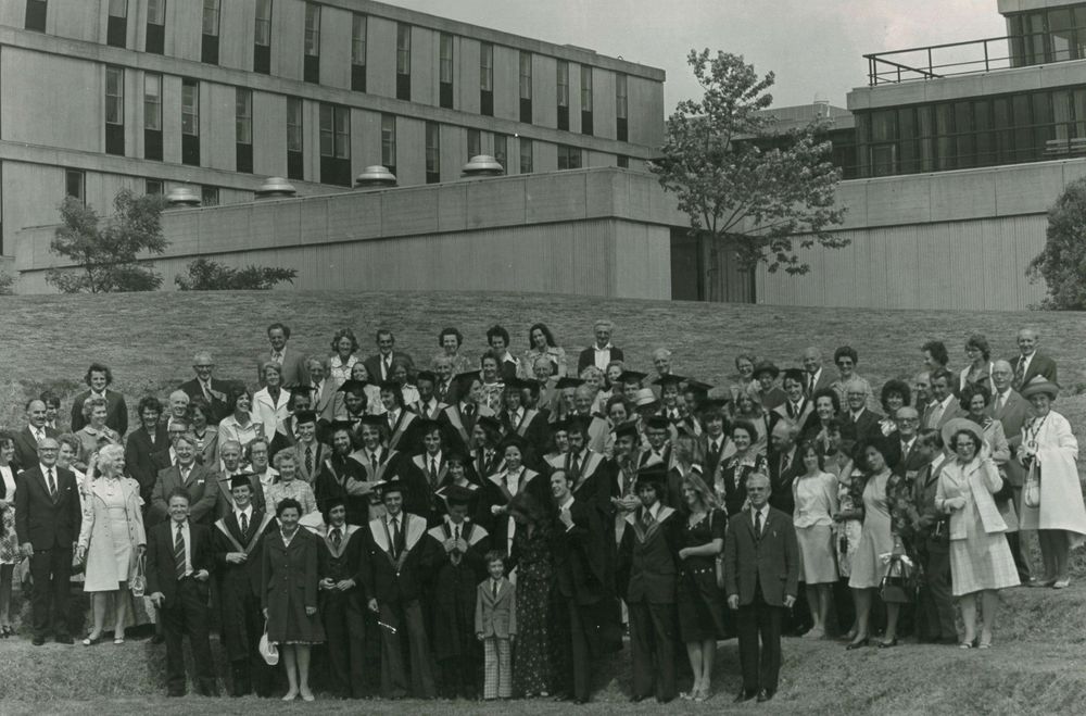 group of graduating students and families posed in a group on the University of Bath campus. Black and white photo. 1970s fashions.