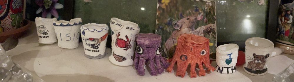 8 shrunken styrofoam cups with various designs including a purple octopus, a red squid, and a pika
