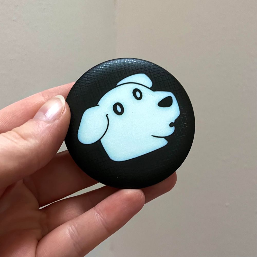 Front design of a magnet bottle opener being held in the artist’s hand. It’s a 2.2 inch diameter magnet design featuring Ghost Dog from my comic Ex Academy! 