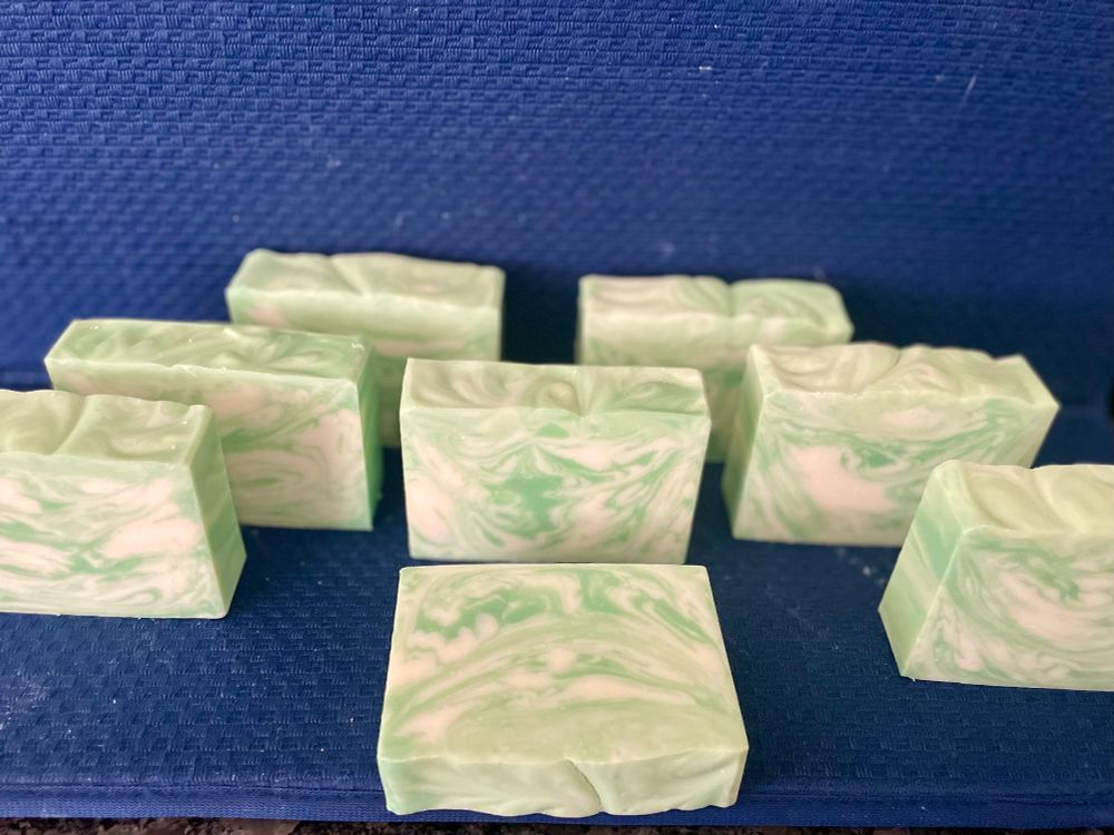 Eight bars of green and white soap sit on a blue mat. The colors are swirled in a wispy, organic way and looking at them, you somehow just know that they are going to feel great on your skin. You can practically smell the scent through the screen. It smells exactly like walking hand-in-hand with your sweetie through an herb garden at twilight, just after a rainstorm. 