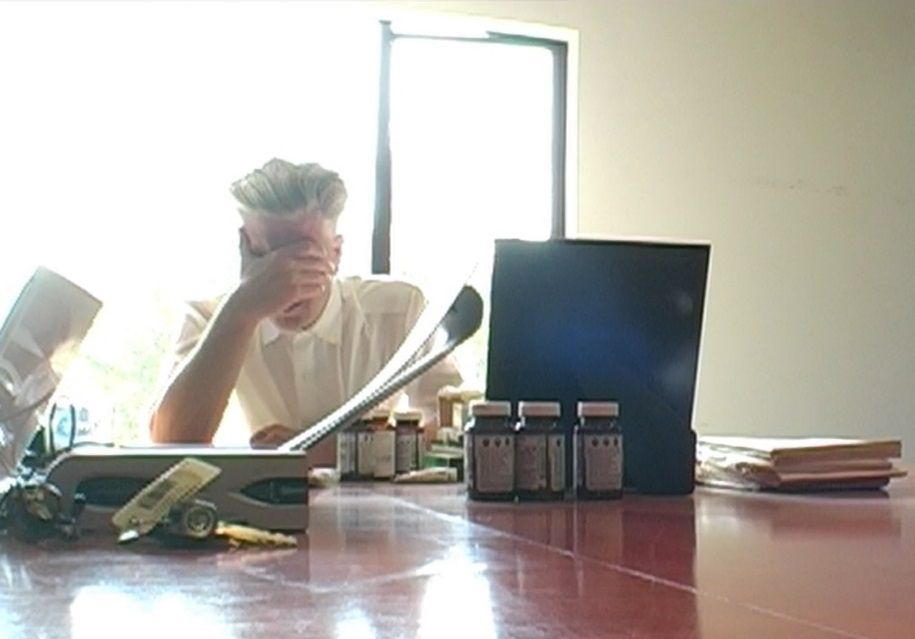 David Lynch sitting around a bunch of pill bottles with his head in his hand