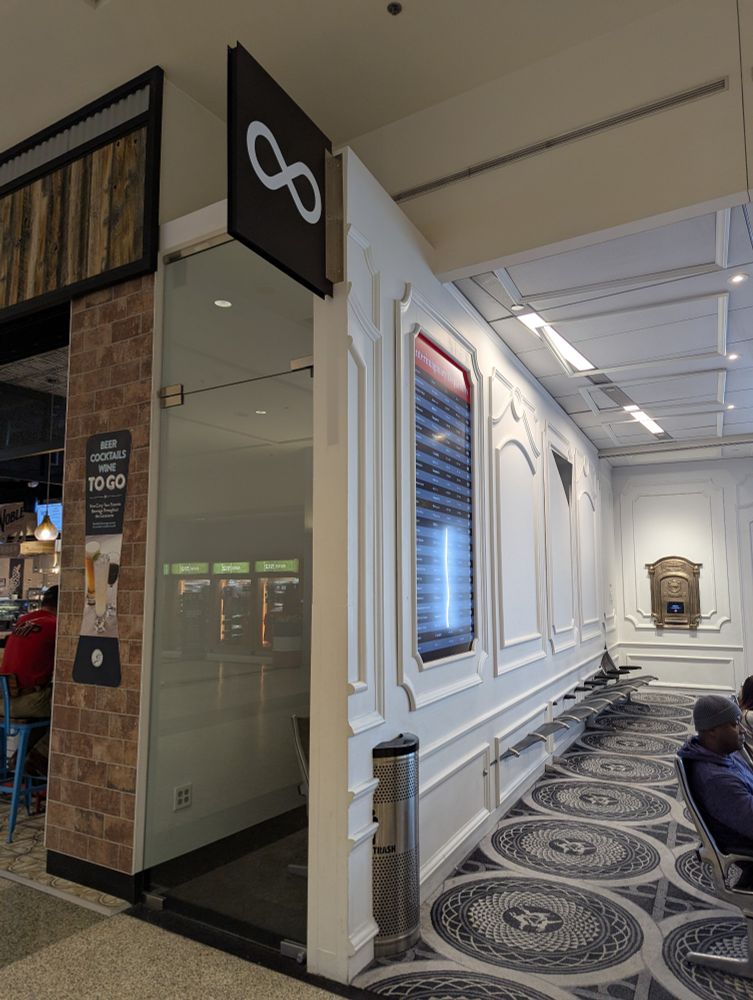 Photo of an art installation at Austin airport consisting of a gate with the number infinity, chairs receding into the wall, and a screen with a flight listing fictional destinations