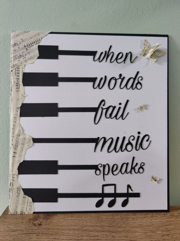A handmade sign saying "when words fail music speaks" in the style of a piano with butterflies made of music paper