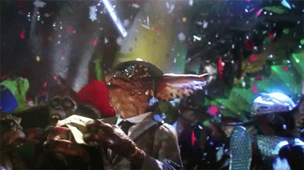 a gremlin in a suit and hat is surrounded by confetti and lights