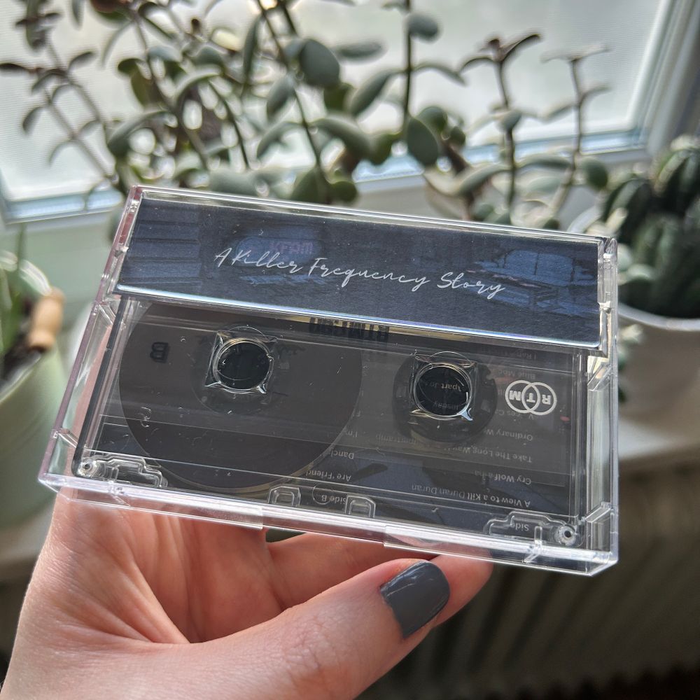 Photo of my hand holding a cassette case turned over, the tape visible under the back flap