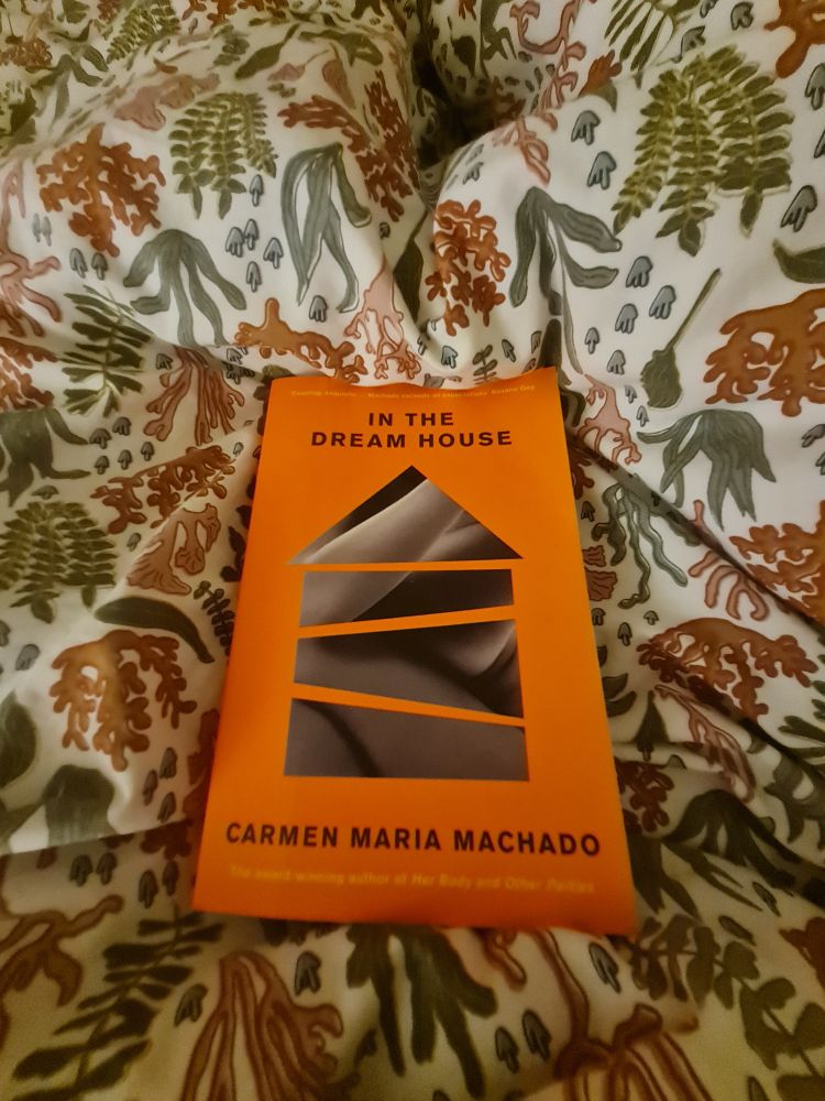 A copy of In The Dream House by Carmen Maria Machado lies on a duvet with sea plants all over.