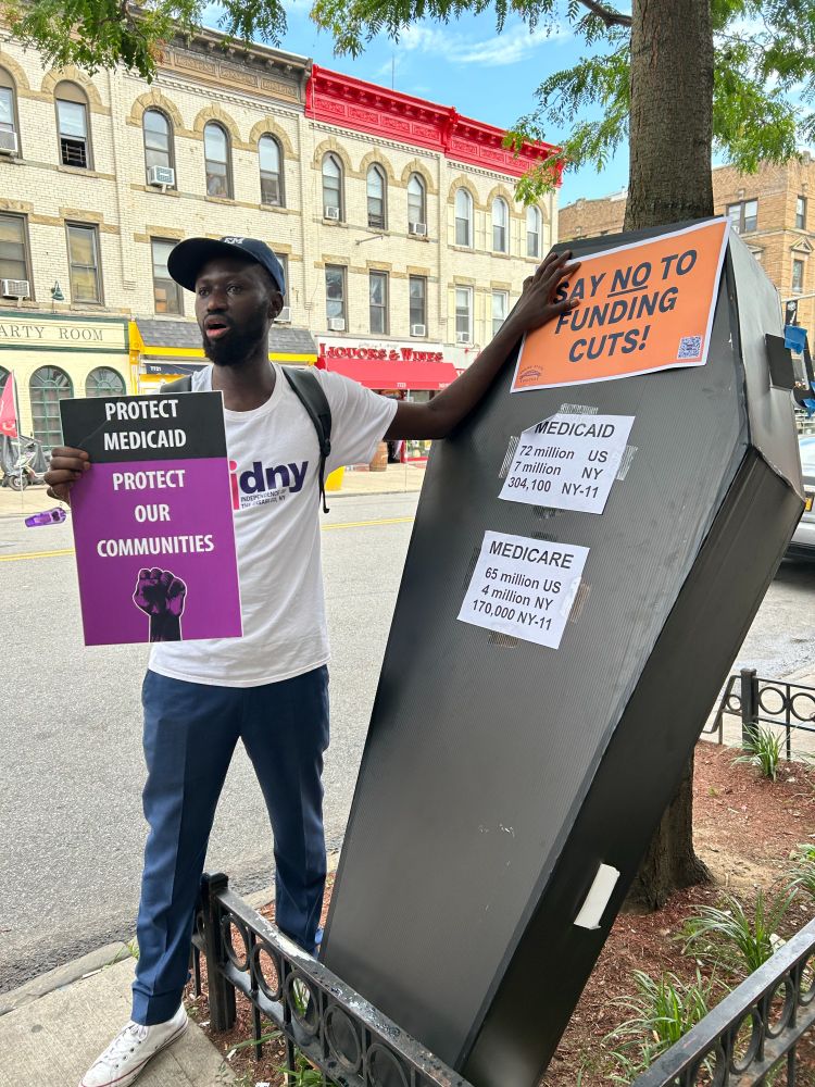 Person holding a sign standing next to a cardboard coffin with Medicaid statistics. 