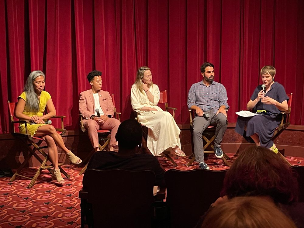 Five people sitting in a panel at a movie theater in front of a red curtain