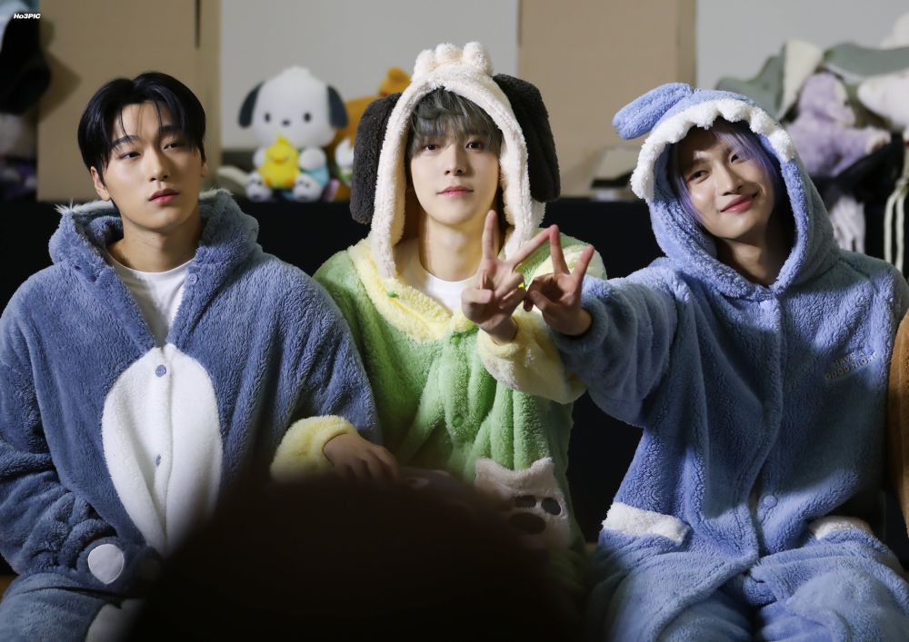 kpop group ateez members (l to r) choi san, jeong yunho, and park seonghwa posing in plush toy themed onesies
