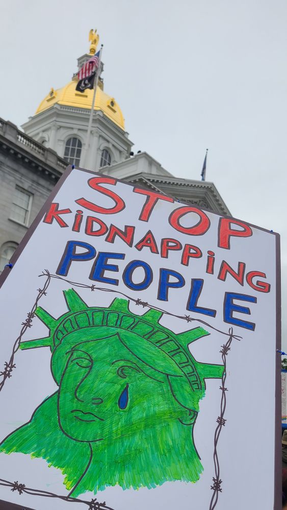 A poster that says "Stop Kidnapping People" in red and blue text at the top, with a picture of the Statue of Liberty crying, surrounded by barbed wire, at the bottom. The golden dome of the NH State House is in the background.