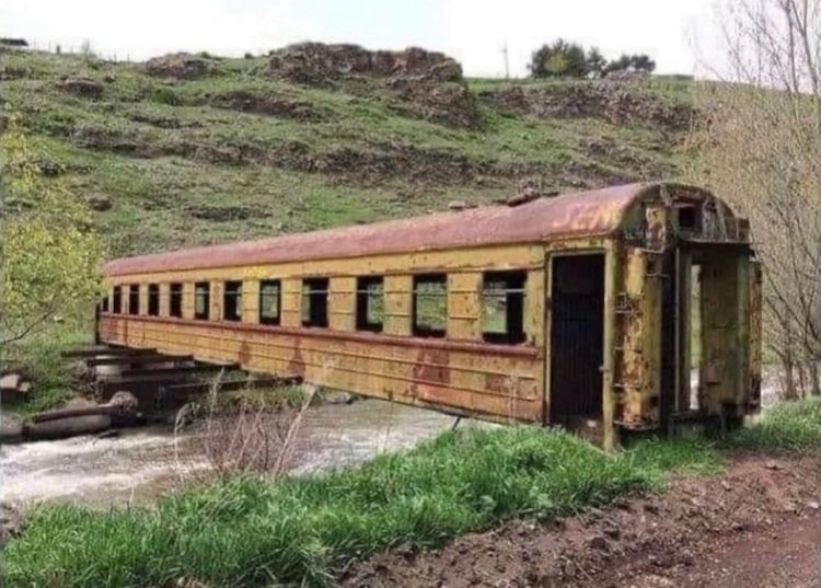 Gångbro, bestående av en rostig gammal tågvagn, över floden Paravani i Georgien.