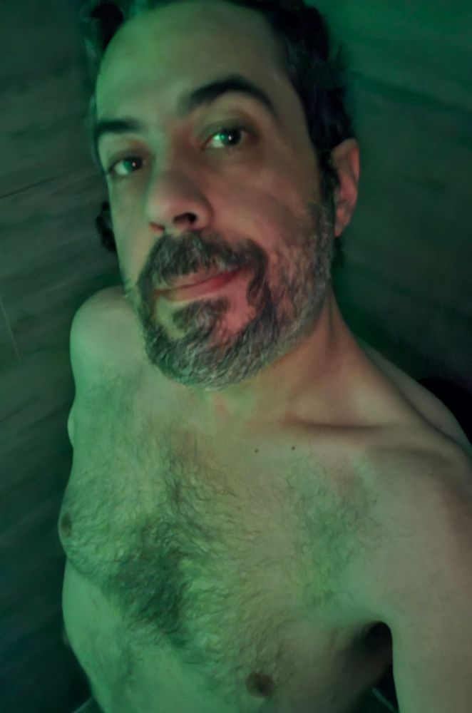 Man lit in green. Naked in shower but visible really only from the waist up. 