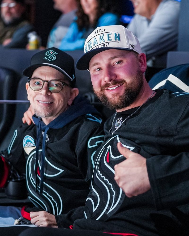 a photo of Seattle Mariners catcher Cal Raleigh posing with a thumbs up in a Seattle Kraken third jersey.