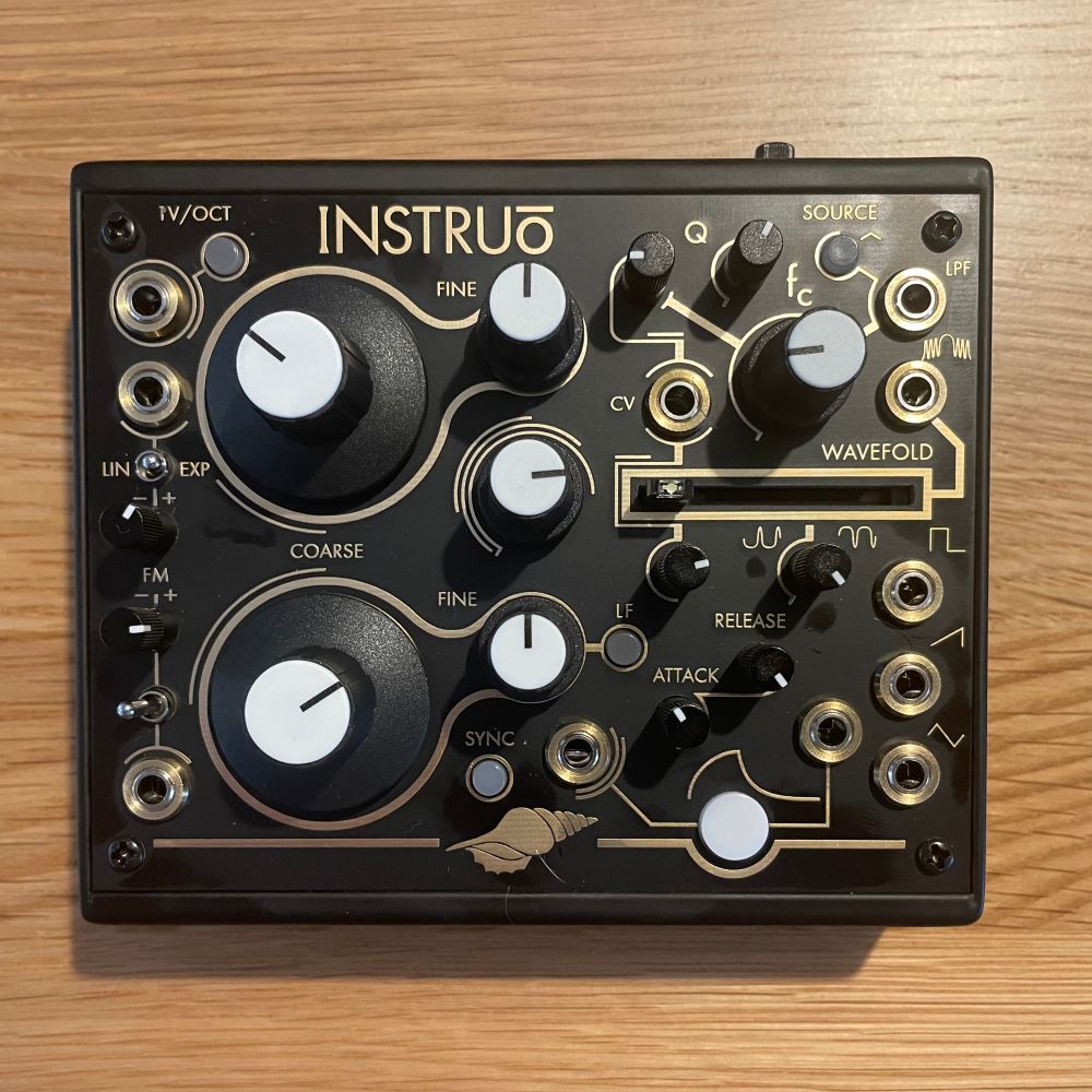 Top down photo of an Instruo Seashell synthesizer. It is square shaped with black and gold colouring, and a lot of different knobs, switches and sliders