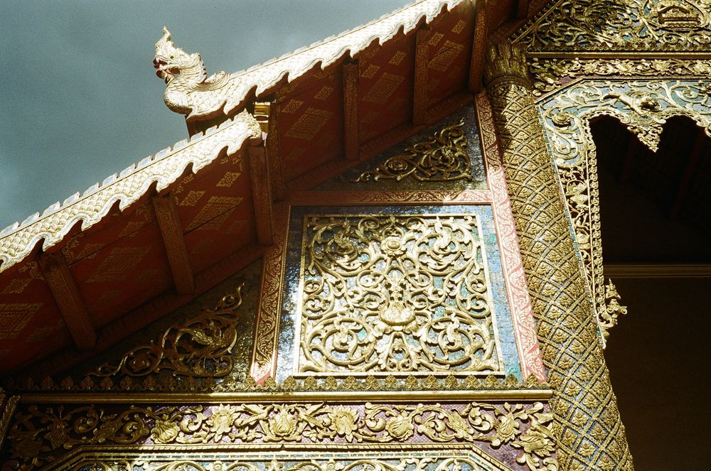 The gleaming architectural details of a Buddhist temple against a dark storm cloud 