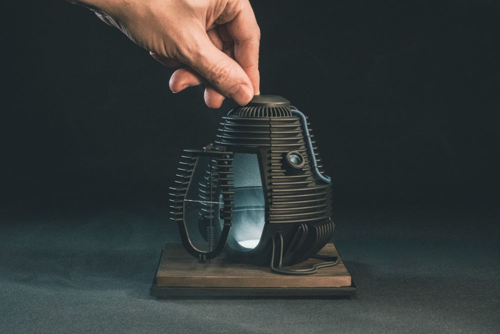 A miniature scaled version of the telepod from the 1986 movie The Fly over a black background. A regular sized hand is at the top of the frame. 
