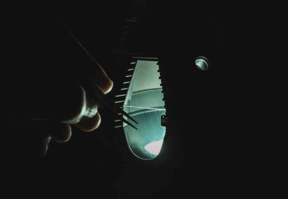 A miniature version of the Telepod from the movie The Fly in a dark room, a normal sized hand on the left holding  tweezers