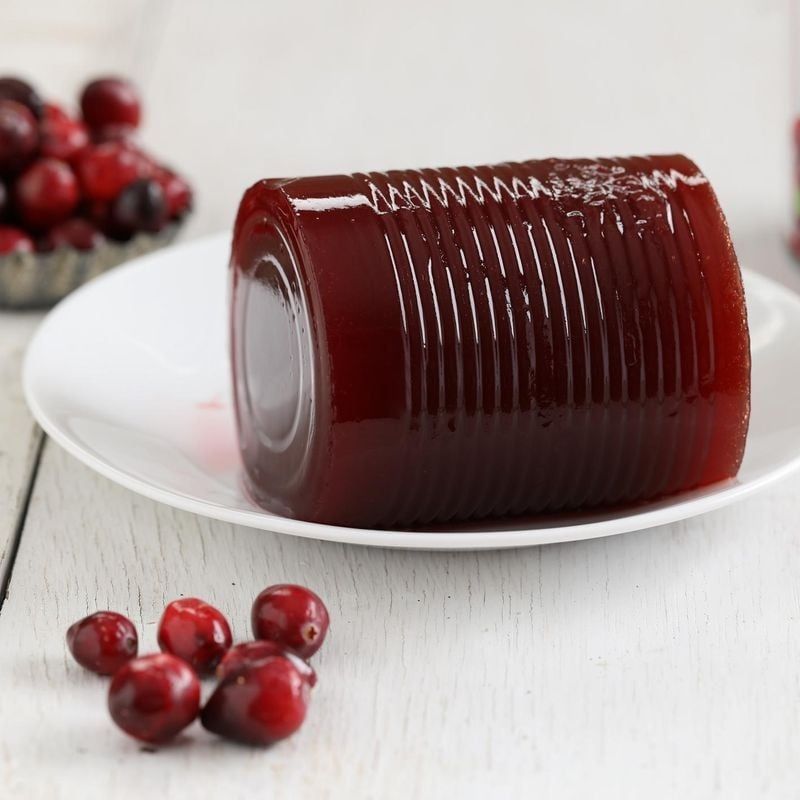 A photo of cranberry sauce (the solid, can-shaped kind) in a dish with some fresh cranberries beside it on the table 