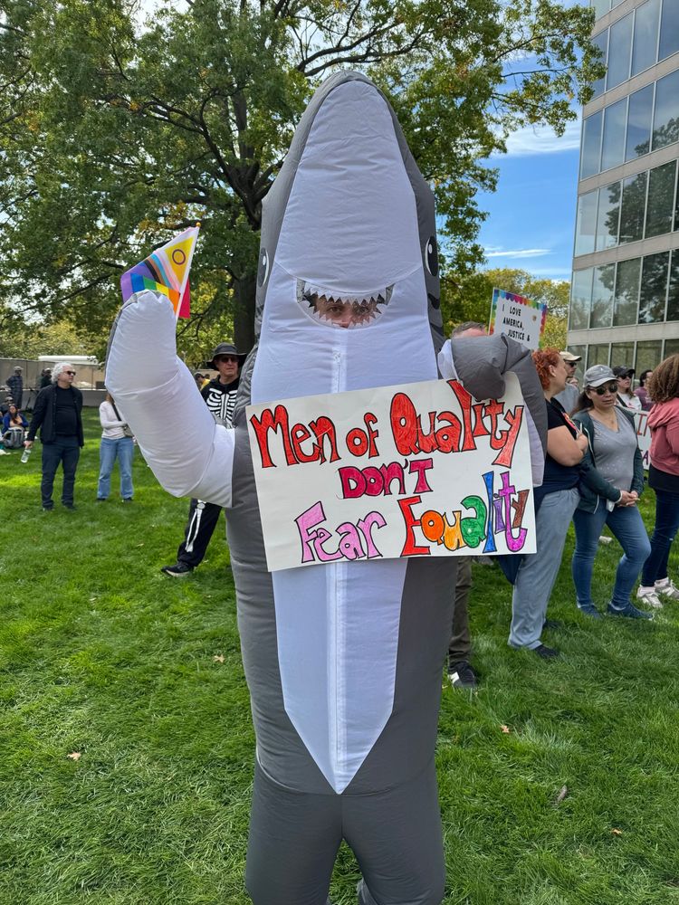 Inflatable shark holding poster that says, “Men of Quality don’t fear Equality”