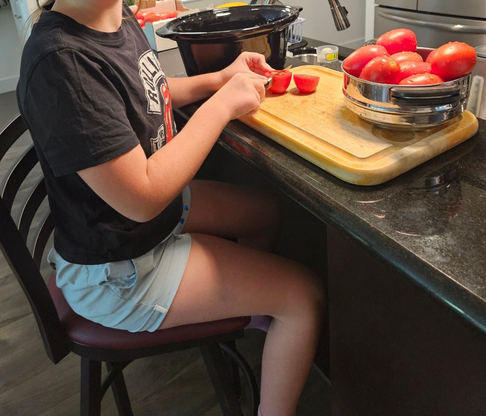 Young girl in black top and blue shorts sitting cutting tomatoes