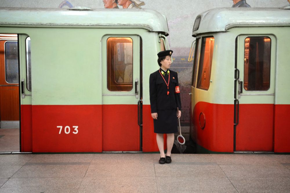 Subway trains at an underground station with a conductor standing on the platform. 