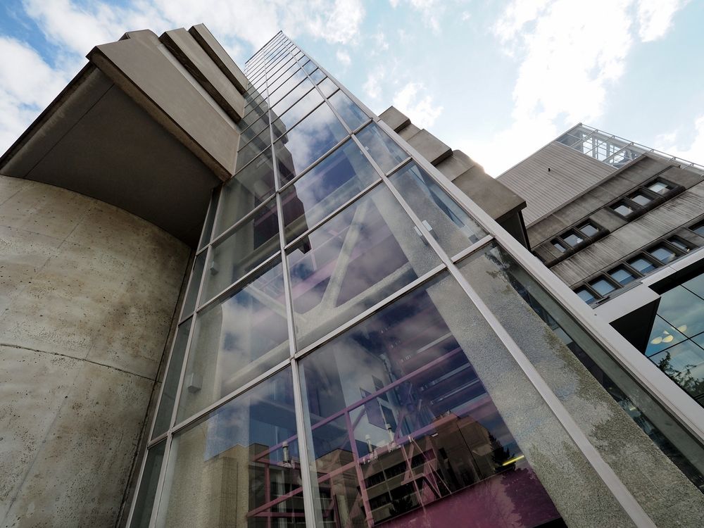 Looking up at a building made of raw concrete, steel and glass built in a Brutalist architecture style,  that emerged in the mid-1900s characterized by “raw concrete” 
massive, geometric shapes looking like a fortress.