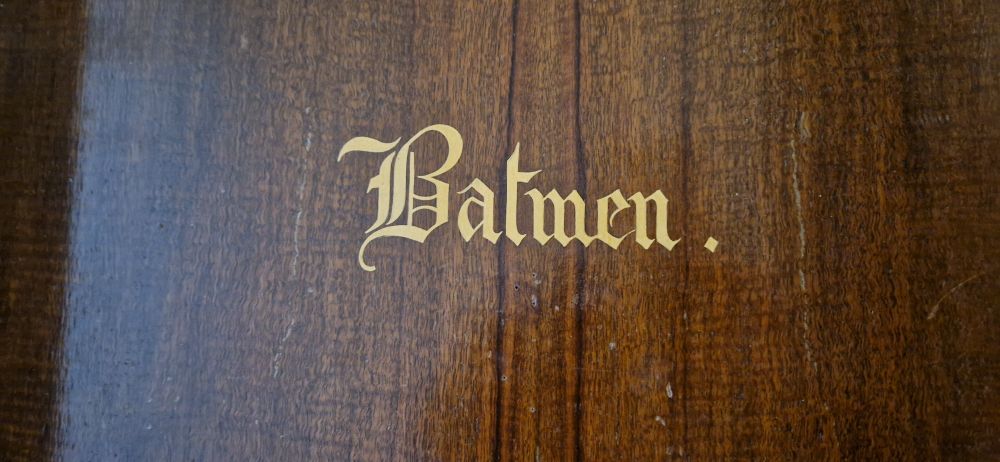 A dark wooden door that says 'Batmen' on it in a fancy gold font. 