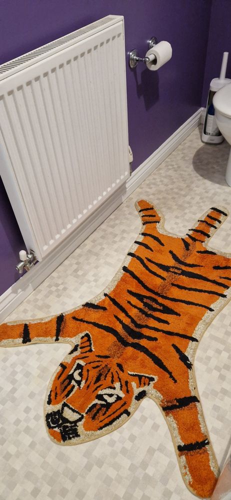 A purple bathroom with an orange 'tigerskin' bathmat on a lino floor. 
