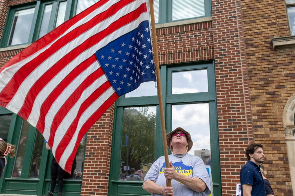 A photograph of a gentleman waving a large upside-down American flag.