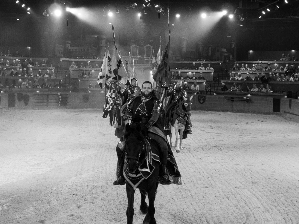 A black and white photograph of the knights of Medieval Times in the arena, riding straight towards the camera.