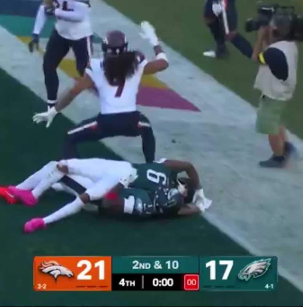 Eagles WRs Brown and Smith lay in a pile with time expired after not making the winning Hail Mary catch.  Broncos Safety Hufanga squats over the pile in celebration.