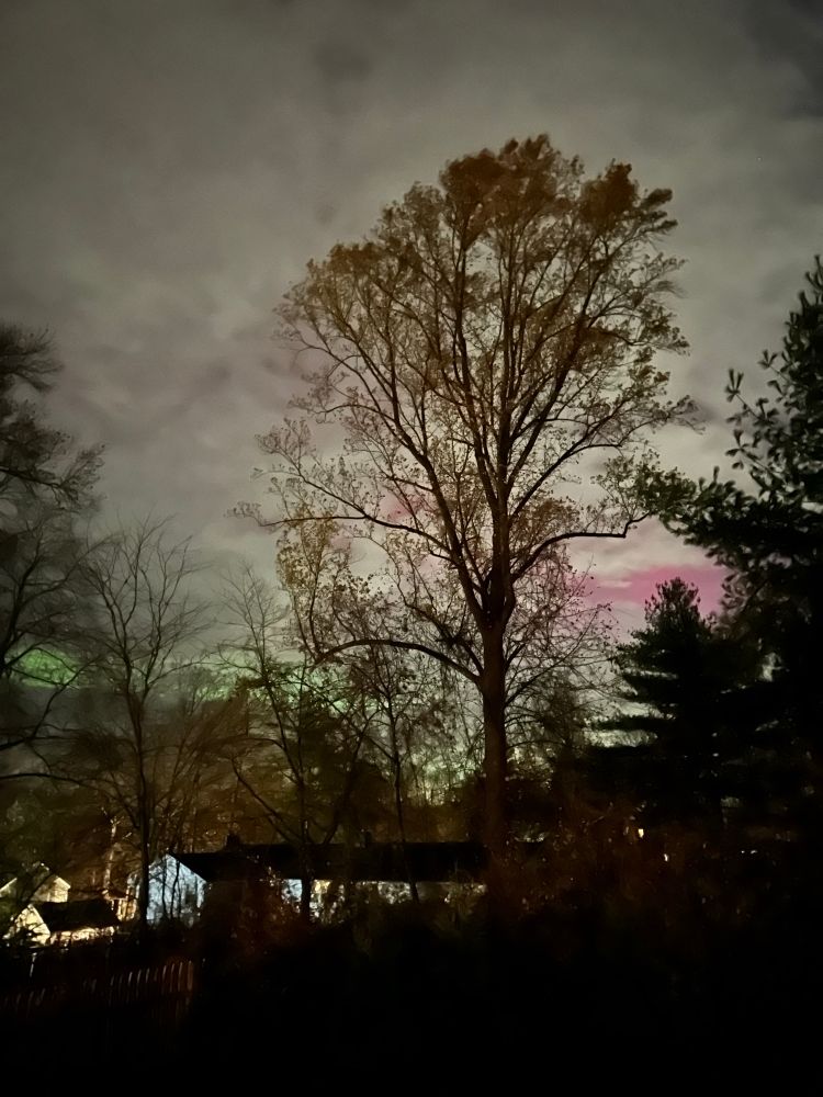 Photo of night sky with aurora borealis greens and pinks visible low on the horizon