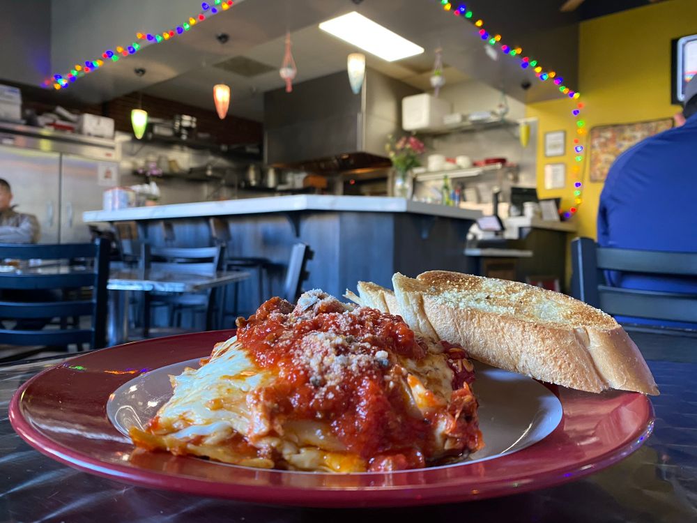 Plate of lasagna and garlic bread with the restaurant counter in the background