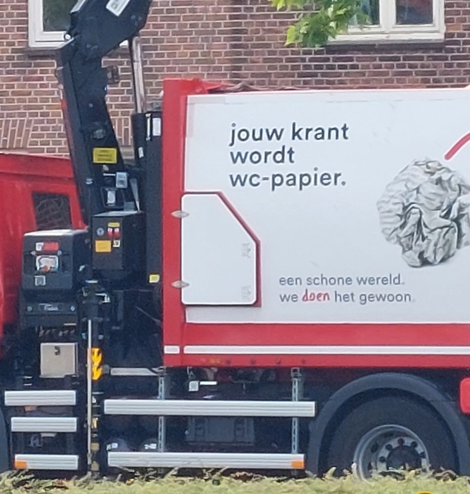 een grote afvalwagen op straat met aan de zijkant de slogan:
'jouw krant wordt wc-papier'