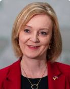 Head and shoulders image of Liz Truss wearing a red jacket and a pendant of a circle in a gold-coloured material.